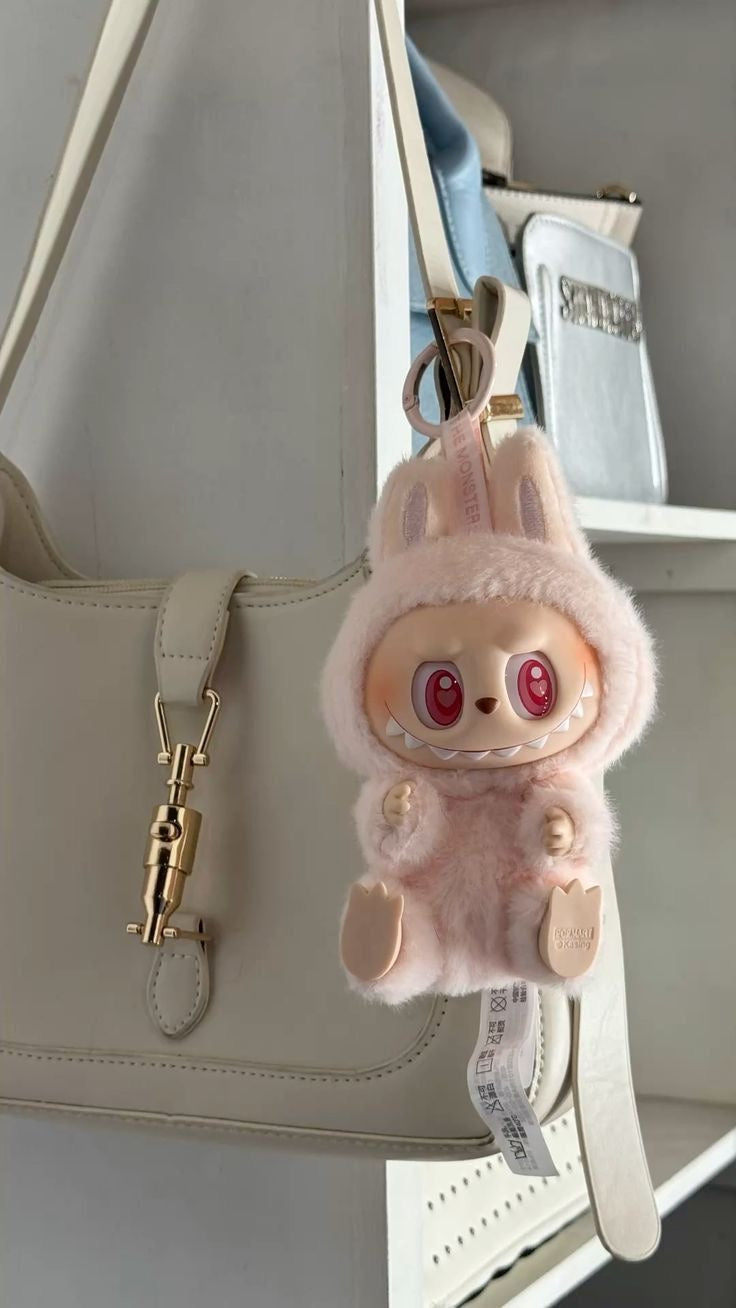 Fluffy pink keychain with a cartoon face attached to a beige handbag.