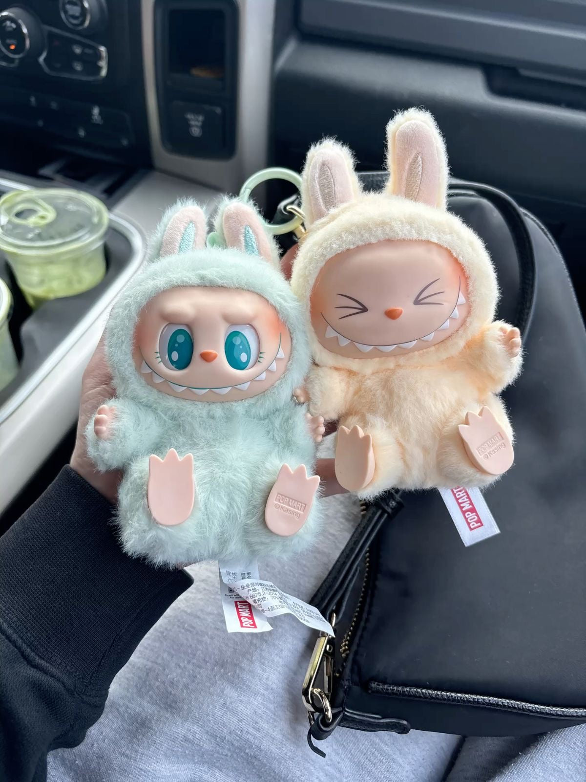 Two plush toys with bunny ears held in front of a car interior.
