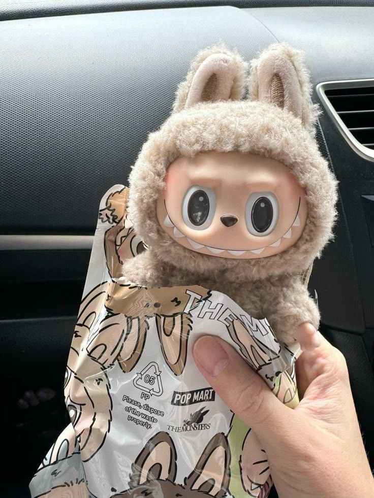Plush toy with cartoon face and butterfly wings held by a hand against a car interior background